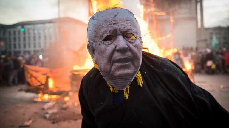 Un participant au carnaval de Marseille affublé d'un masque de Jean-Claude Gaudin, le maire de la ville, pose devant une statut de ce dernier à laquelle il a été mis le feu, le 10 mars 2019
