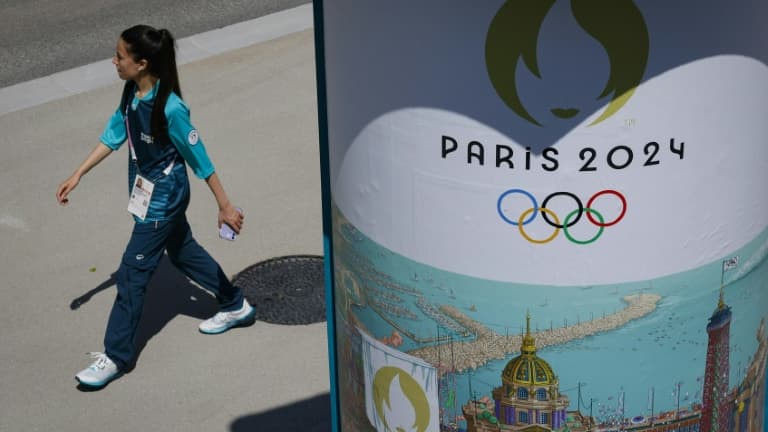 Une volontaire passant à côté d'une affiche des Jeux olympiques 2024 dans le village des athlètes le 18 juillet 2024 à Saint-Denis